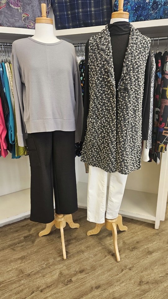 Two mannequins displaying styled outfits at Jorie's Fine Clothing, featuring a grey sweater with black pants and a textured vest with white jeans