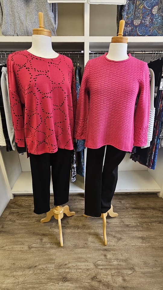 Red patterned sweater and pink textured knit top with black pants on display